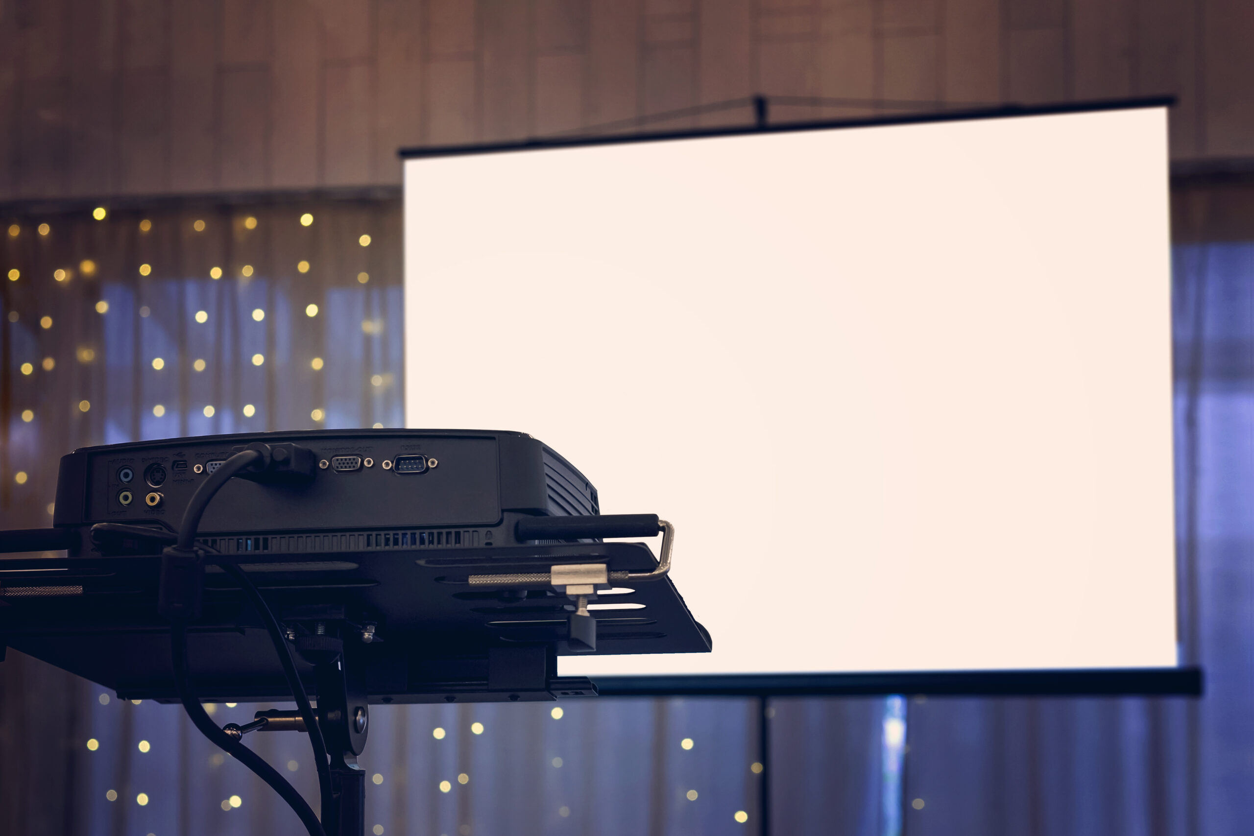 A view to the projection screen equipment at the decorated window curtain background of a banquet hall. Facilities for video and audio projection at a festive event. Show arrangement at a banquet.